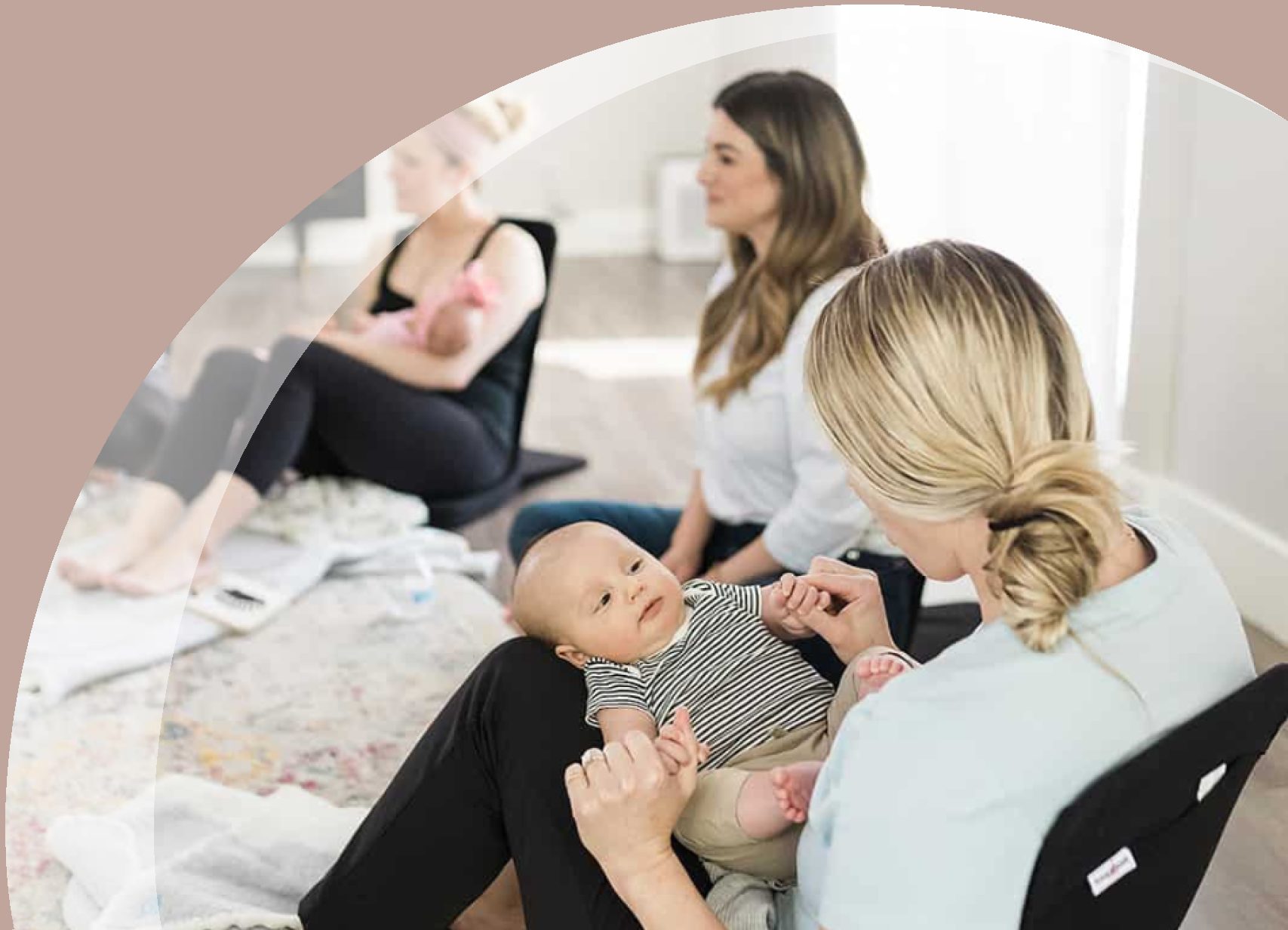 Group of smiling moms sitting with babies on blankets out in front of them on the floor