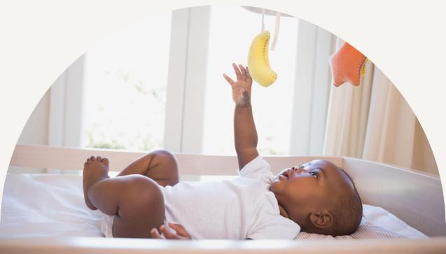 Baby laying on its back playing with a colorful mobile above its head